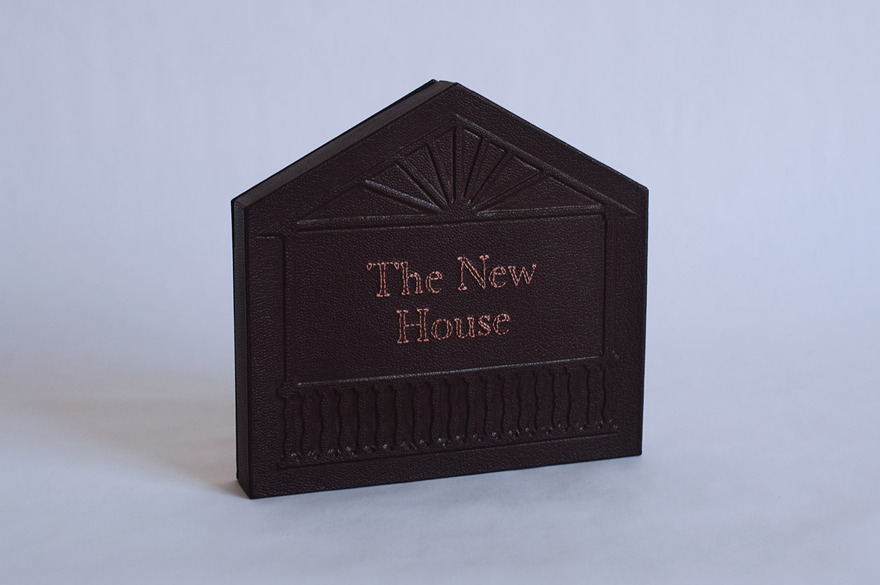 Box front cover of The New House binding on a white table.