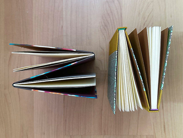 Two variations of the Dos-a-dos Binding standing upright on a wooden table.