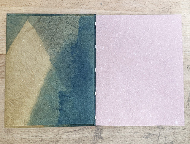 An Envelope Binding with front cover open sitting on wooden table.