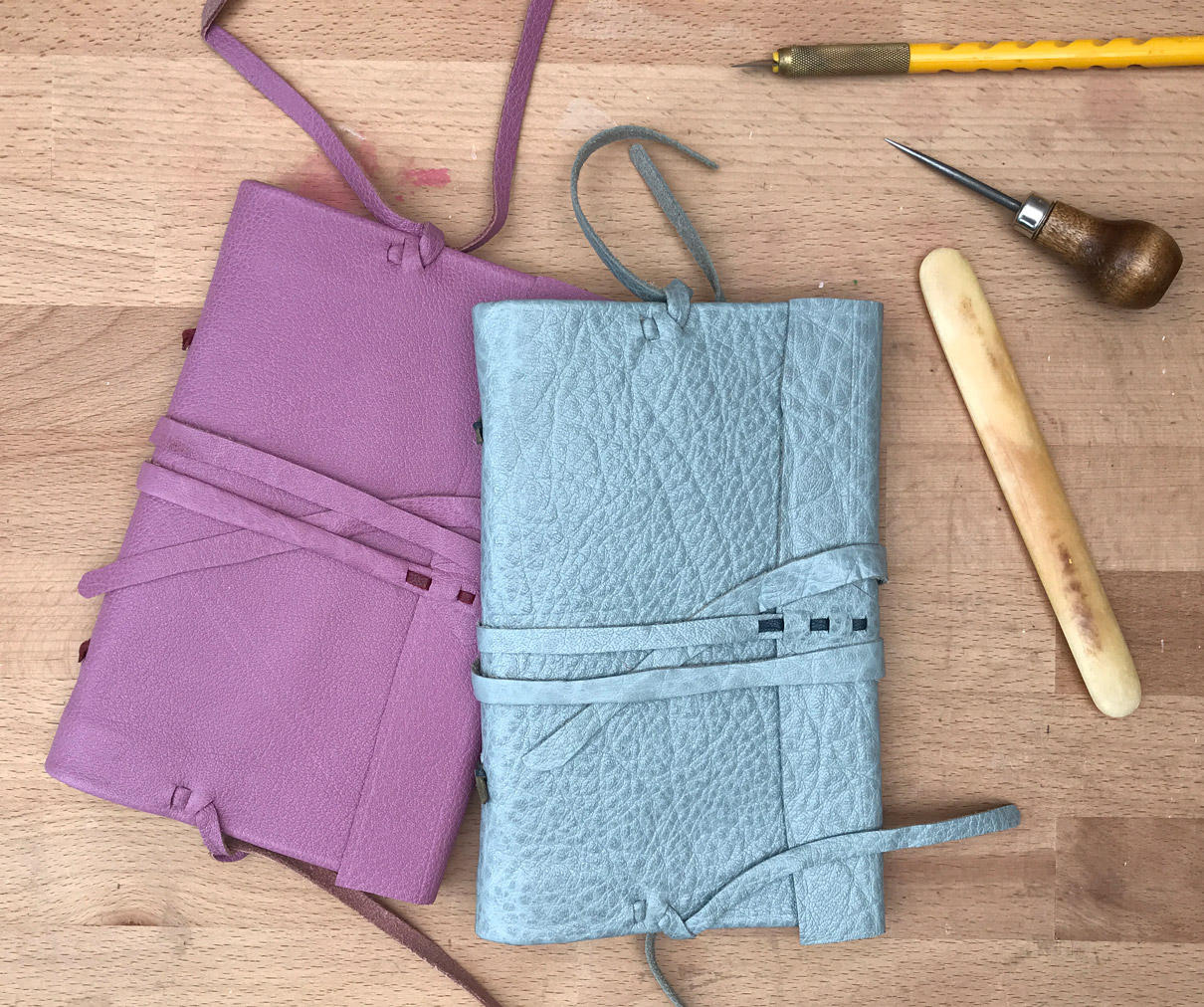 Two modern Nag Hammadi bindings laying on a wooden table with some bookbinding tools.