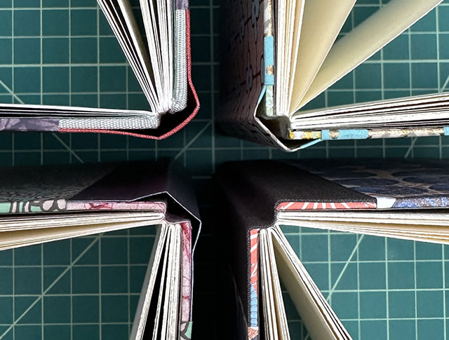Four variations of the Sewn Boards Binding sitting upright on a cutting mat.
