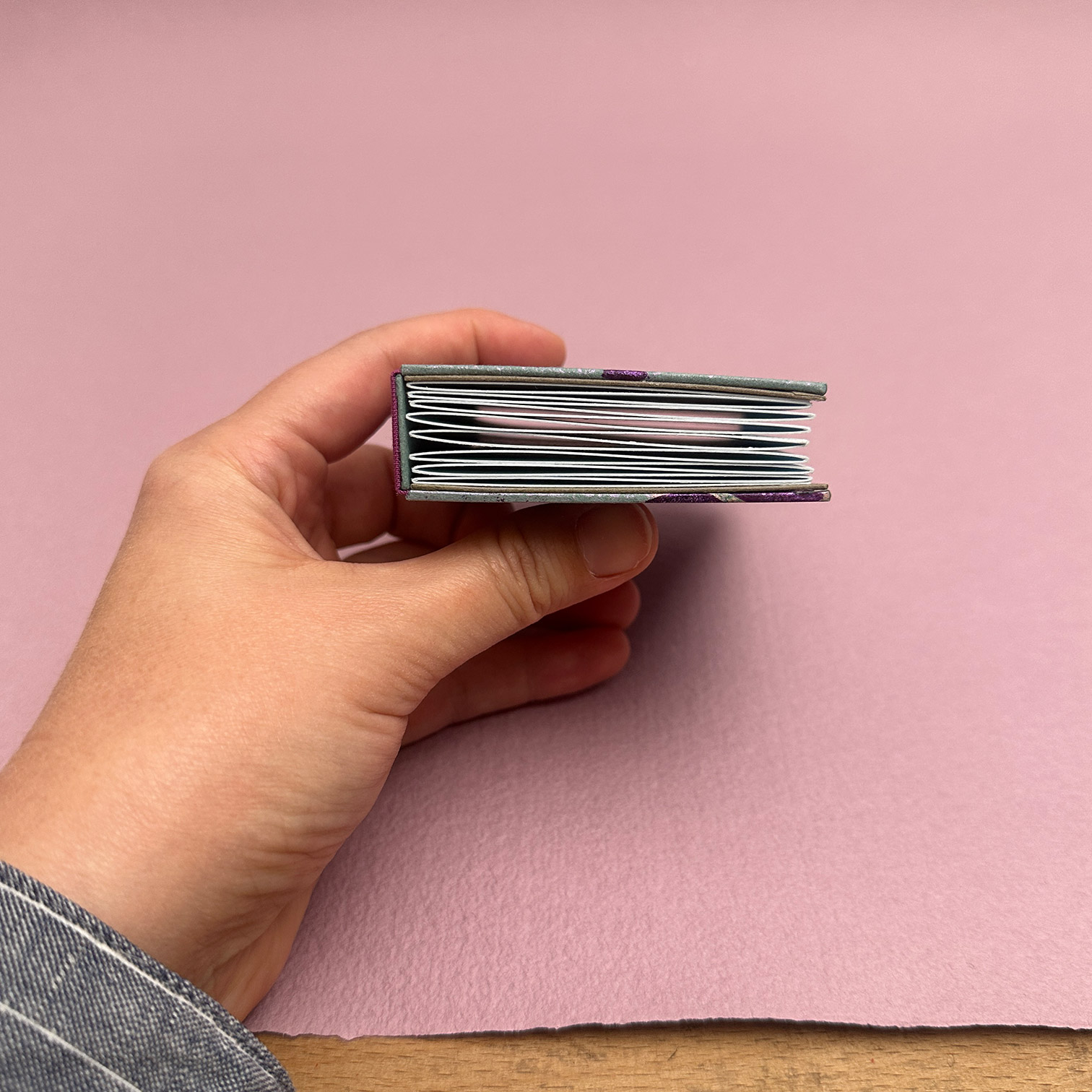 Showing the closed head edge of the double panel binding with lilac handmade paper backdrop.