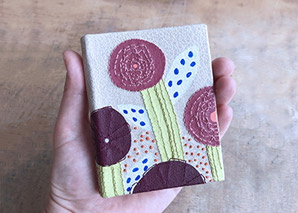 A hand holding a samll embroidered leather binding with flowers on it.