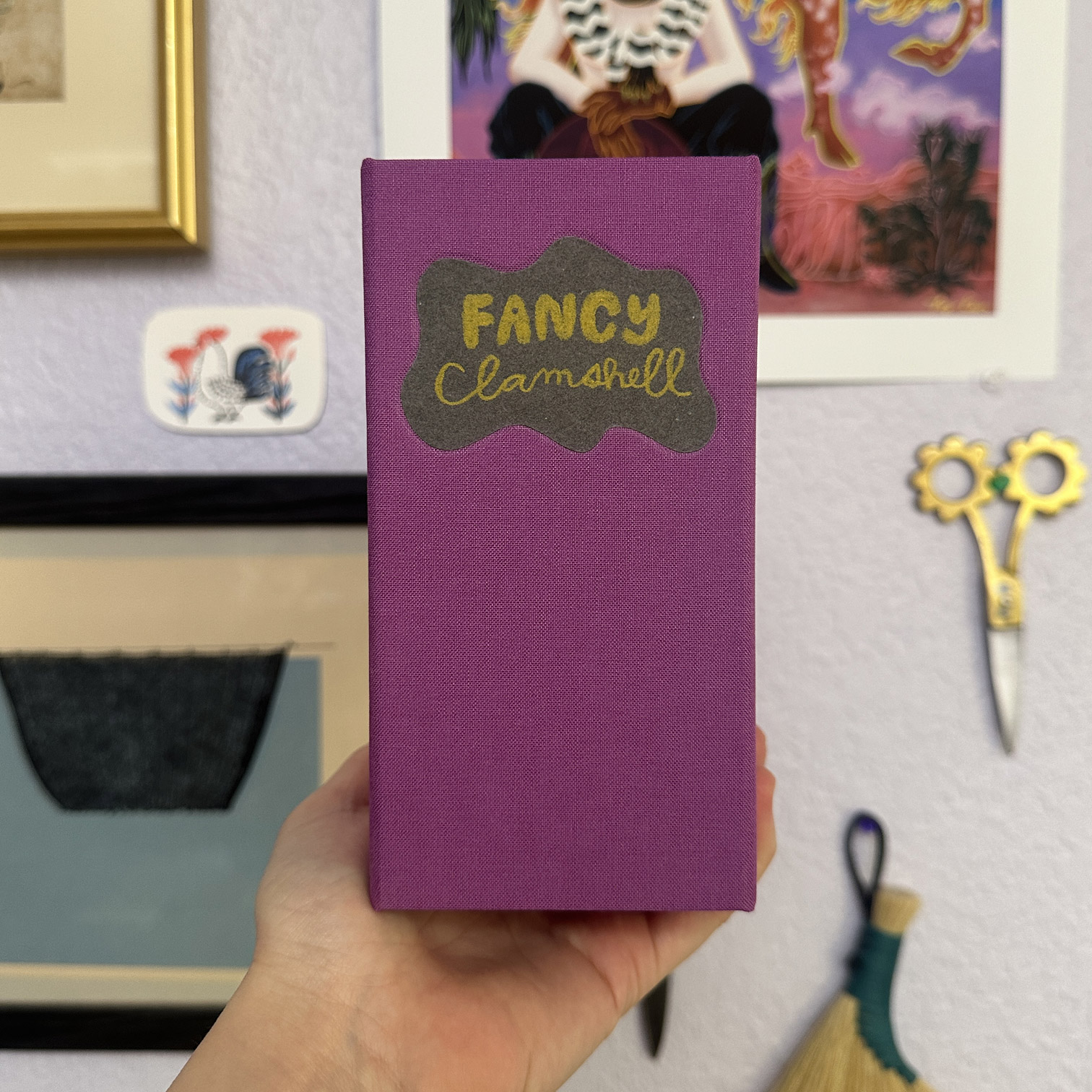 A hand holding up a box with the spine facing forward, label says Fancy Clamshell.