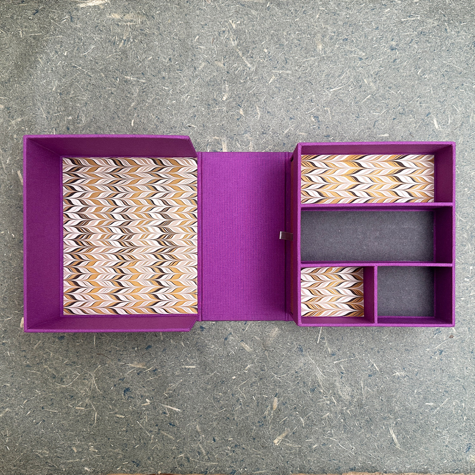A clamshell box fully opened showing a divided compartment lined with marbled paper.