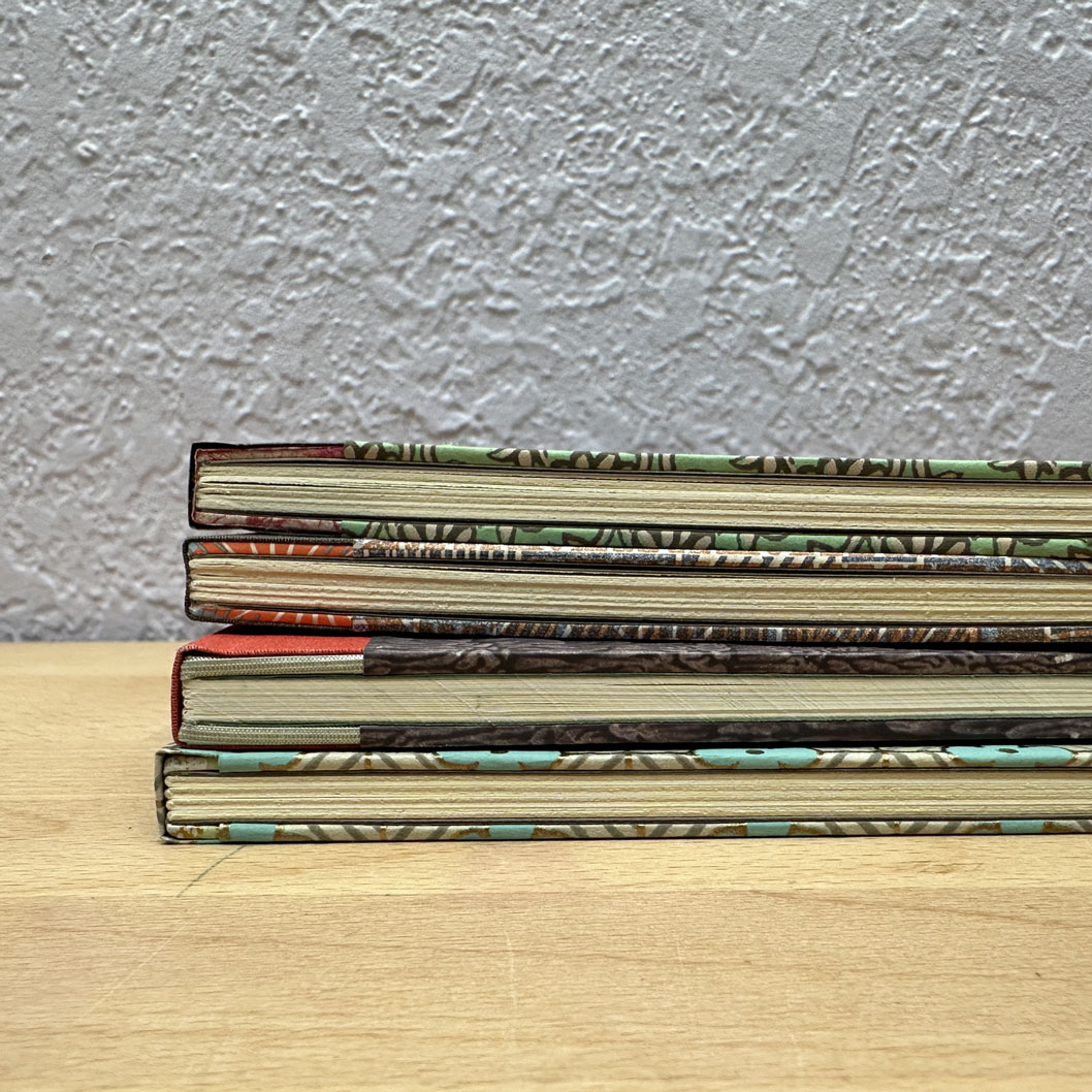 Stack of sewn boards bindings sitting on a wooden table.