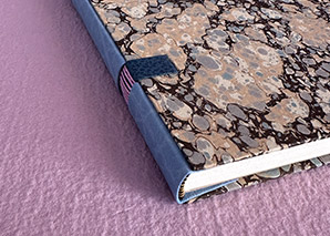 The tail edge of a Sheats binding sitting on a lilac textured paper.